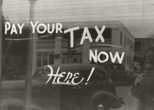 Classic photo of a window reflecting old cars with "pay your tax now here!"