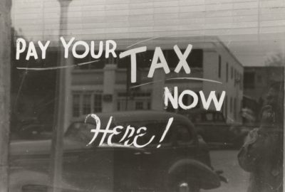 Classic photo of a window reflecting old cars with "pay your tax now here!"